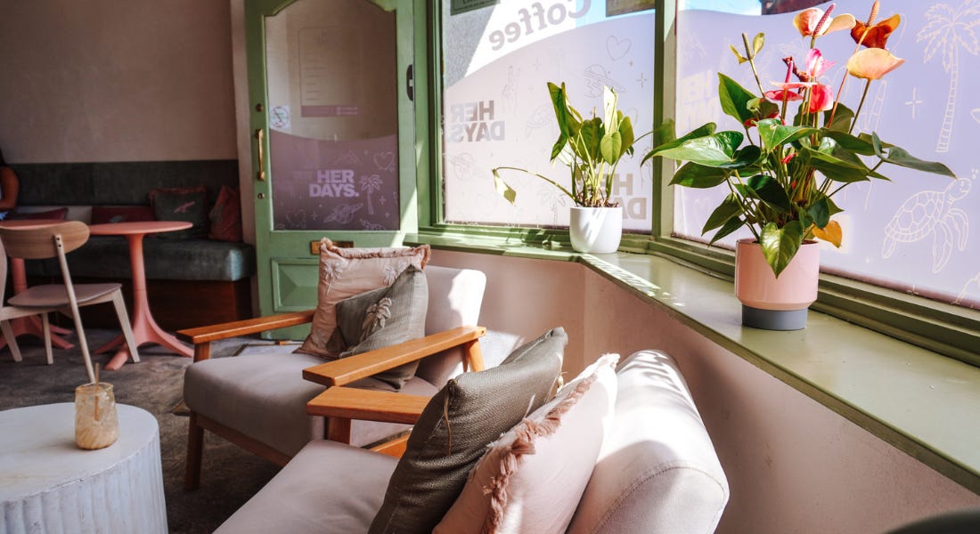 A cafe interior with green and pink seats, a green door and window, and a lily plant A cafe interior with green and pink seats, a green door and window, and a lily plant