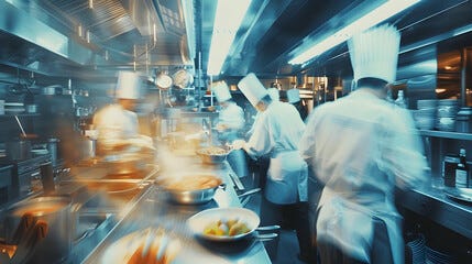 Una cocina ocupada en una foto borrosa por la alta exposición y el movimiento de los cocineros. Una cocina ocupada en una foto borrosa por la alta exposición y el movimiento de los cocineros.
