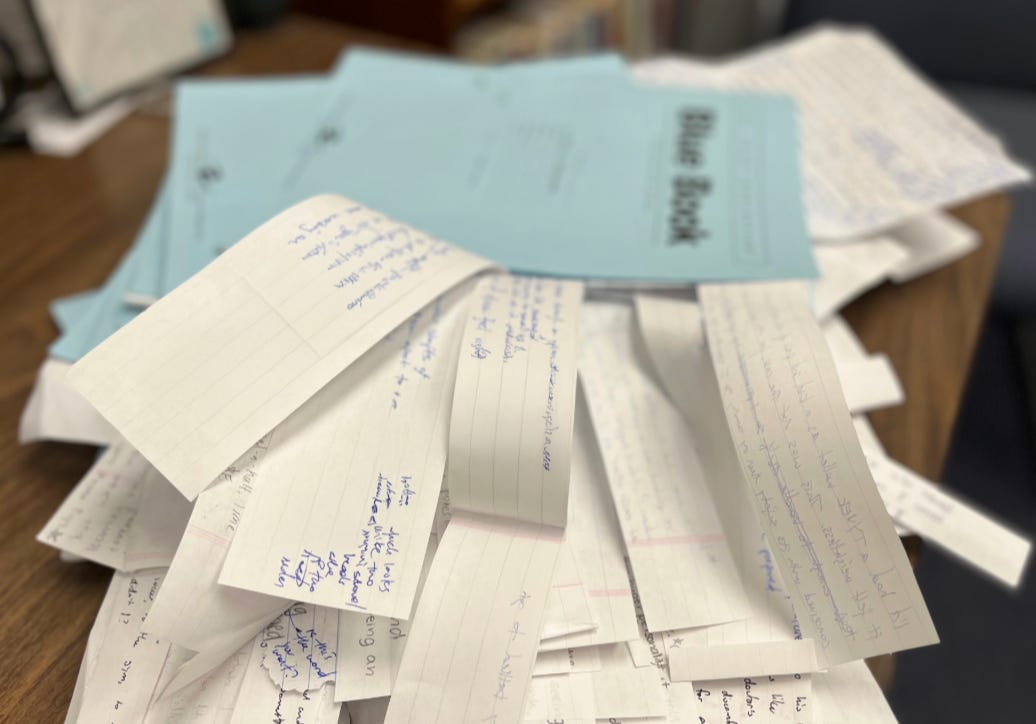 slightly blurred stack of blue books with strips of paper with writing on them sticking out. writing is blurred