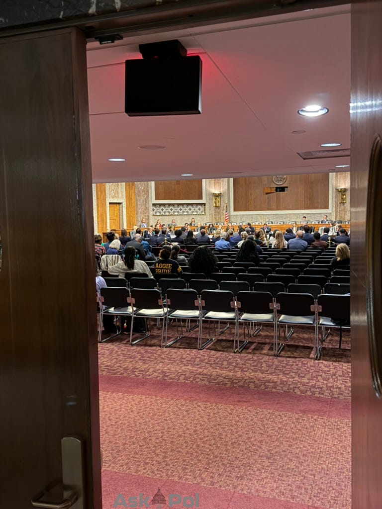 Lawmakers sit on a large wooden dais as a crowd listens to the public hearing they're conducting on ICE shootings