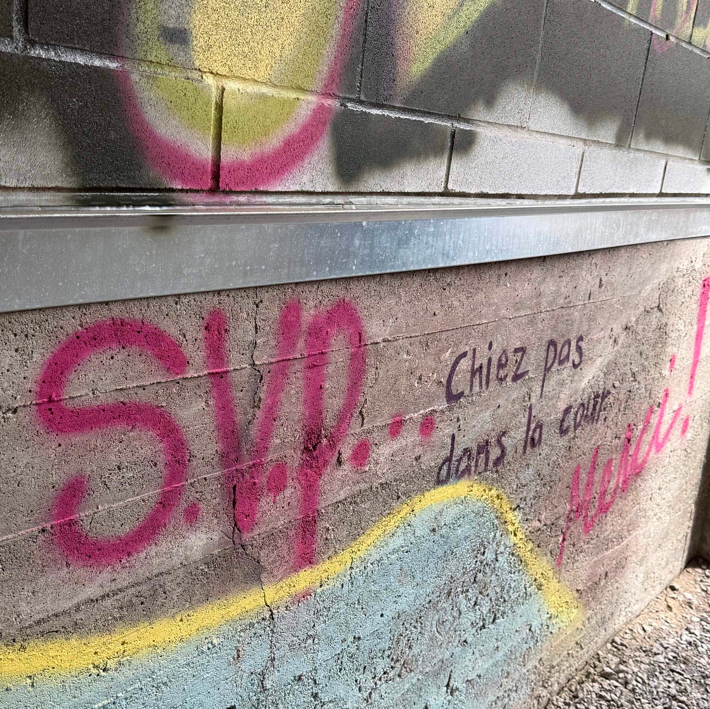 A concrete wall with colorful graffiti. Spray-painted in pink: "S.V.P…" followed in black marker: "Chiez pas dans la cour." Then in pink again: "Merci!"