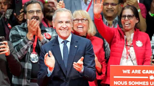 A man smiles and claps as cheering people stand behind him. A man smiles and claps as cheering people stand behind him.