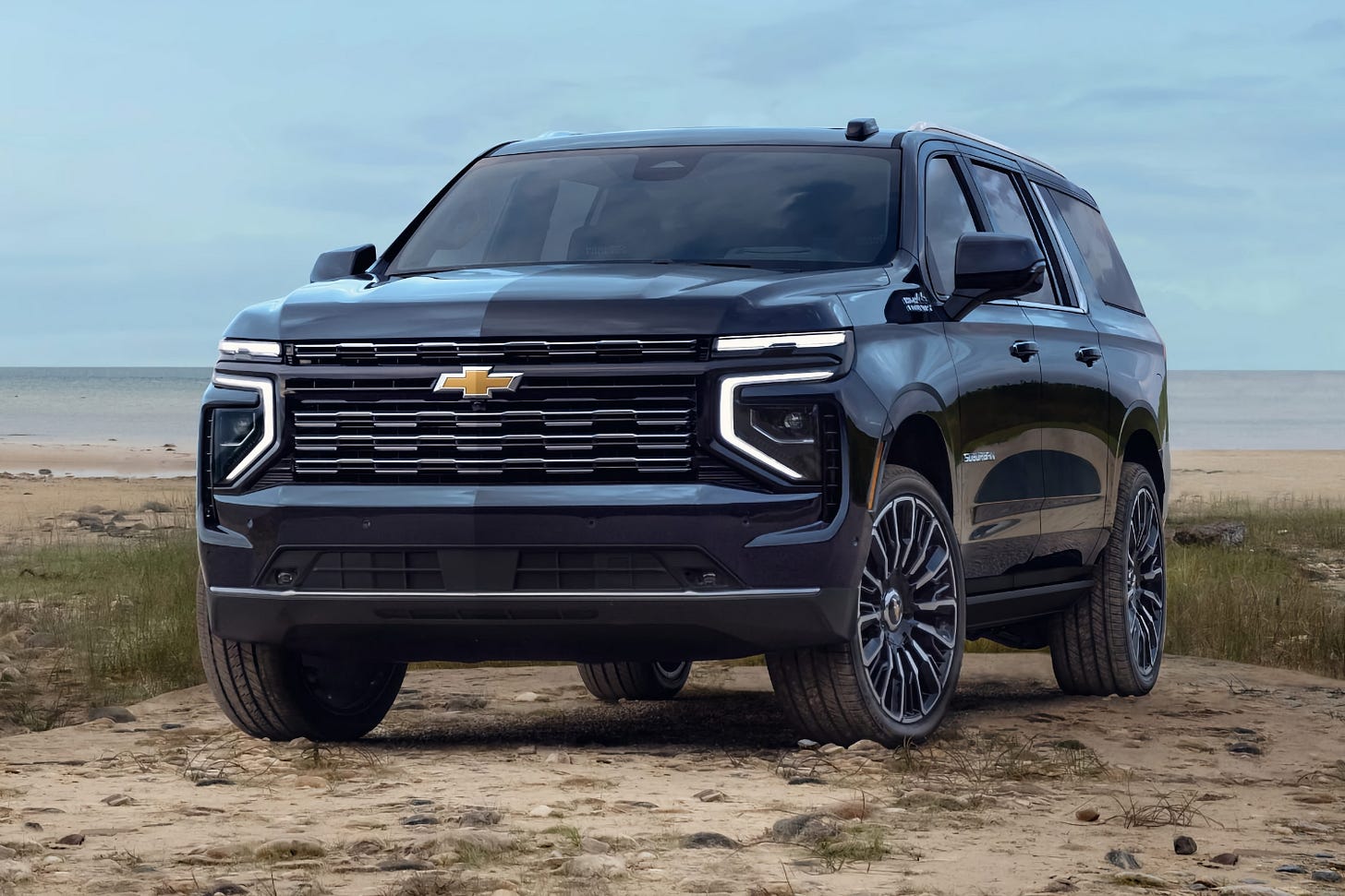 A blue 2025 Chevrolet Suburban High Country equipped with large 24-inch wheels is parked on a beach on the shore of Lake Michigan. A blue 2025 Chevrolet Suburban High Country equipped with large 24-inch wheels is parked on a beach on the shore of Lake Michigan.