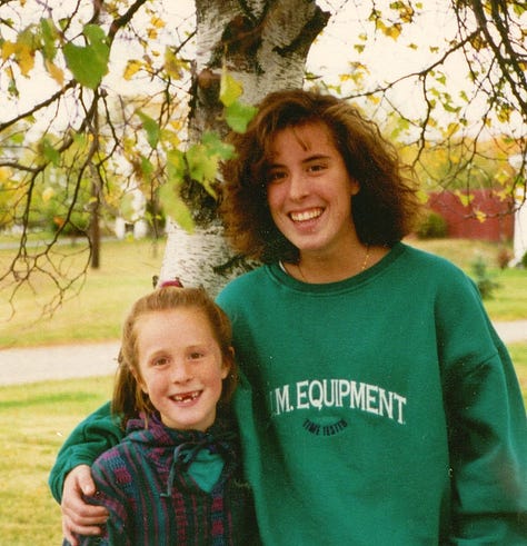 Slide 1: Photo of Andrea in high school with a weird perm and a BUM equipment sweatshirt, arm around their little sister who is missing teeth. Slide 2: Andrea with a radical haircut - long on top with shaved sides, a feather boa, and a tank top that says "love me anyways". Slide 3: Andrea standing against a column with a rainbow painted on it.