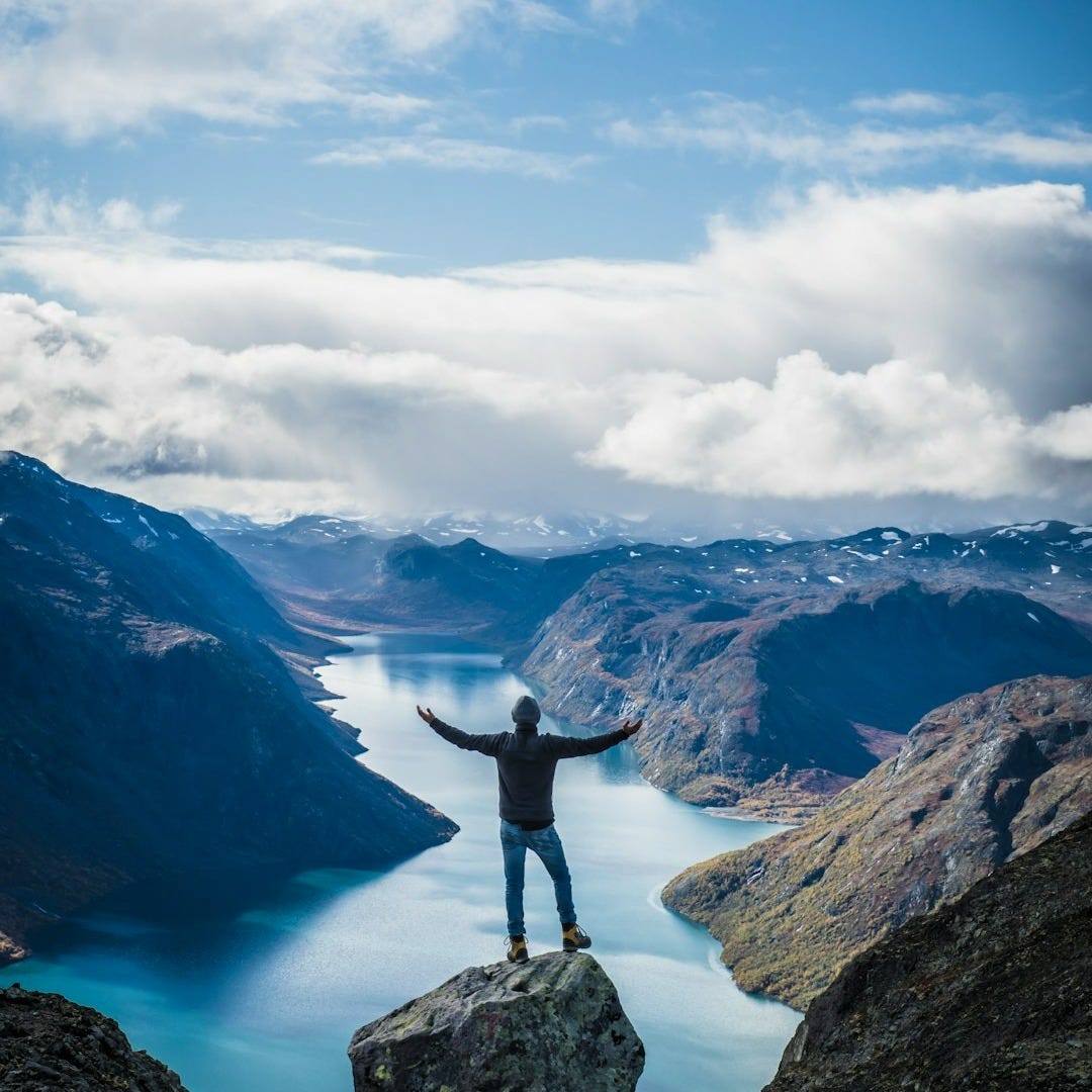 person standing on rock formation near mountains under white clouds during daytime person standing on rock formation near mountains under white clouds during daytime