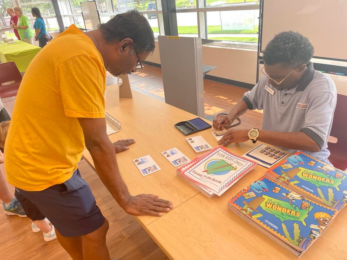 A man watching another man apply a postmark to envelopes A man watching another man apply a postmark to envelopes