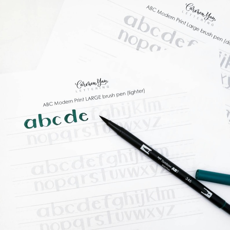 May include: A close-up of a brush pen writing the alphabet in a modern print style. The pen is black with a green cap and the letters are written in a dark green ink. The text "ABC Modern Print LARGE brush pen (lighter)" is visible at the top of the image.