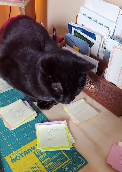 a black cat sits on a crowded desk amid a field of post-it notes