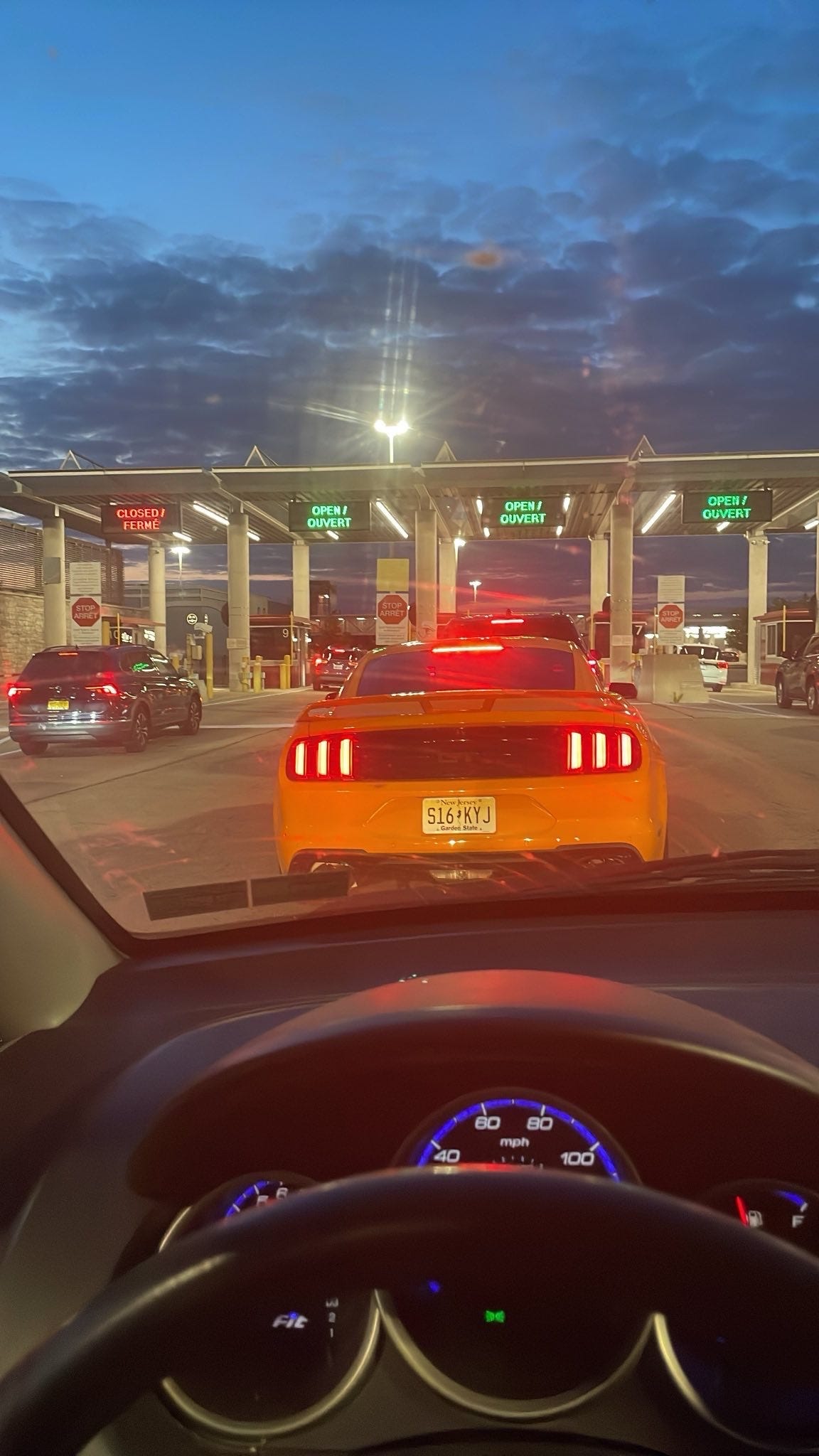 an image of the Canadian land border, a yellow camaro from New Jersey is in front of the car where the shot is taken, there is a twilight sky and many drive through lanes