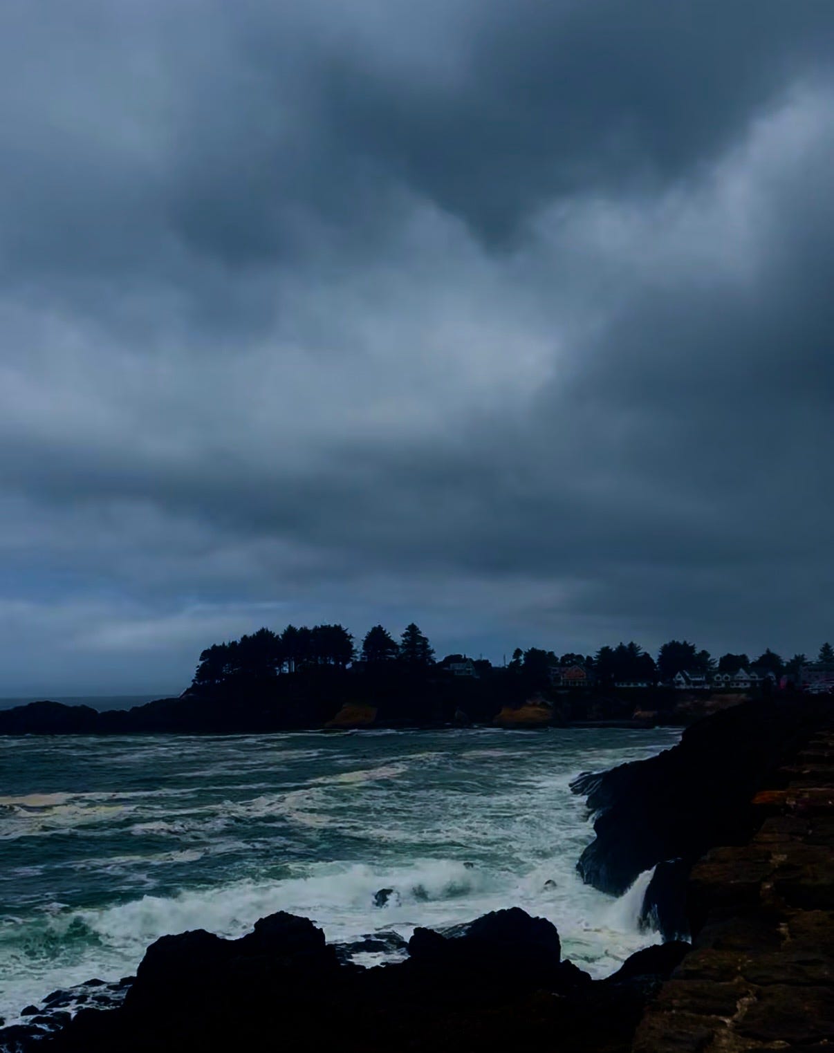 Stormy, overcast sky above a rocky Oregon coastline with waves crashing against dark cliffs and a narrow stone path along the edge. Stormy, overcast sky above a rocky Oregon coastline with waves crashing against dark cliffs and a narrow stone path along the edge.