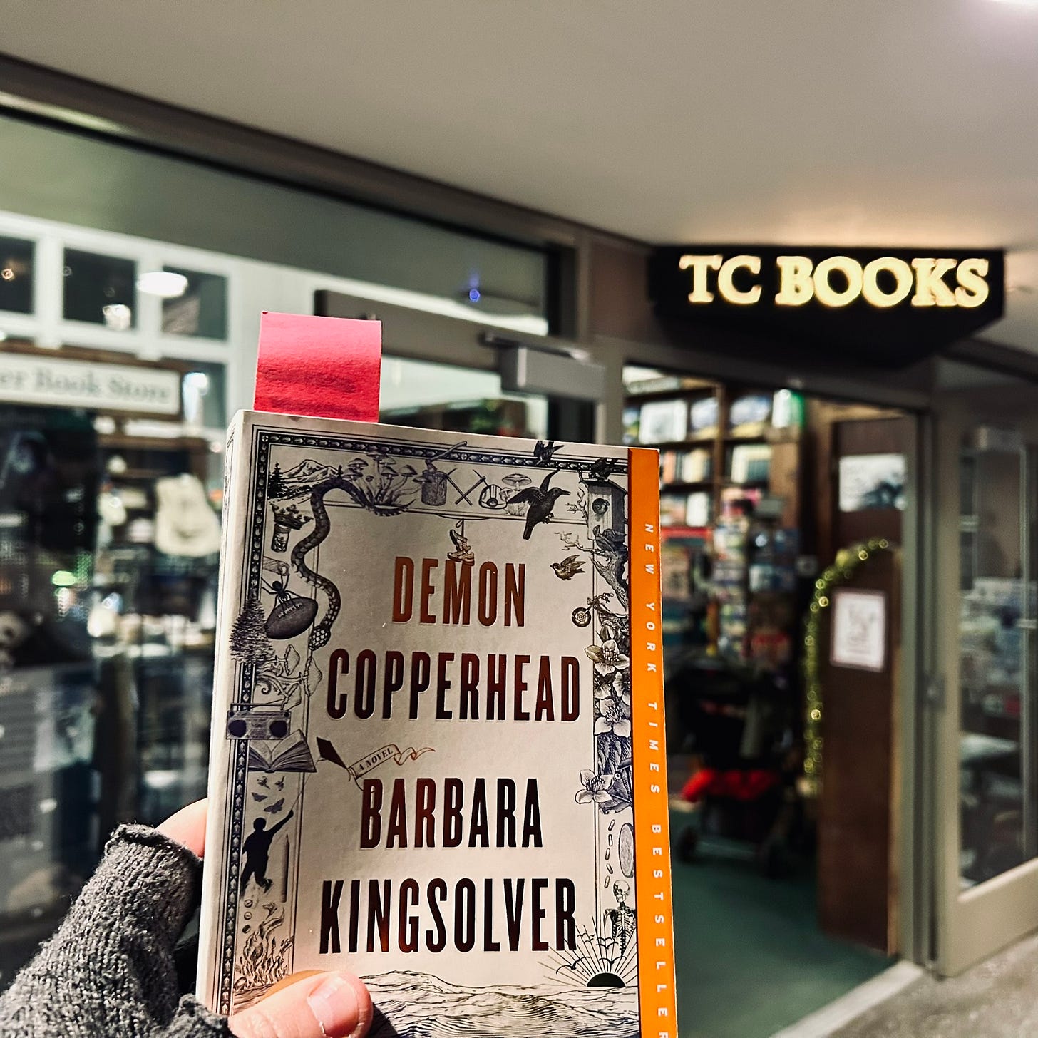A hand holding up a copy of Barbara Kingsolver's "Demon Copperhead" in front of the Tattered Cover bookstore in Denver Union Station