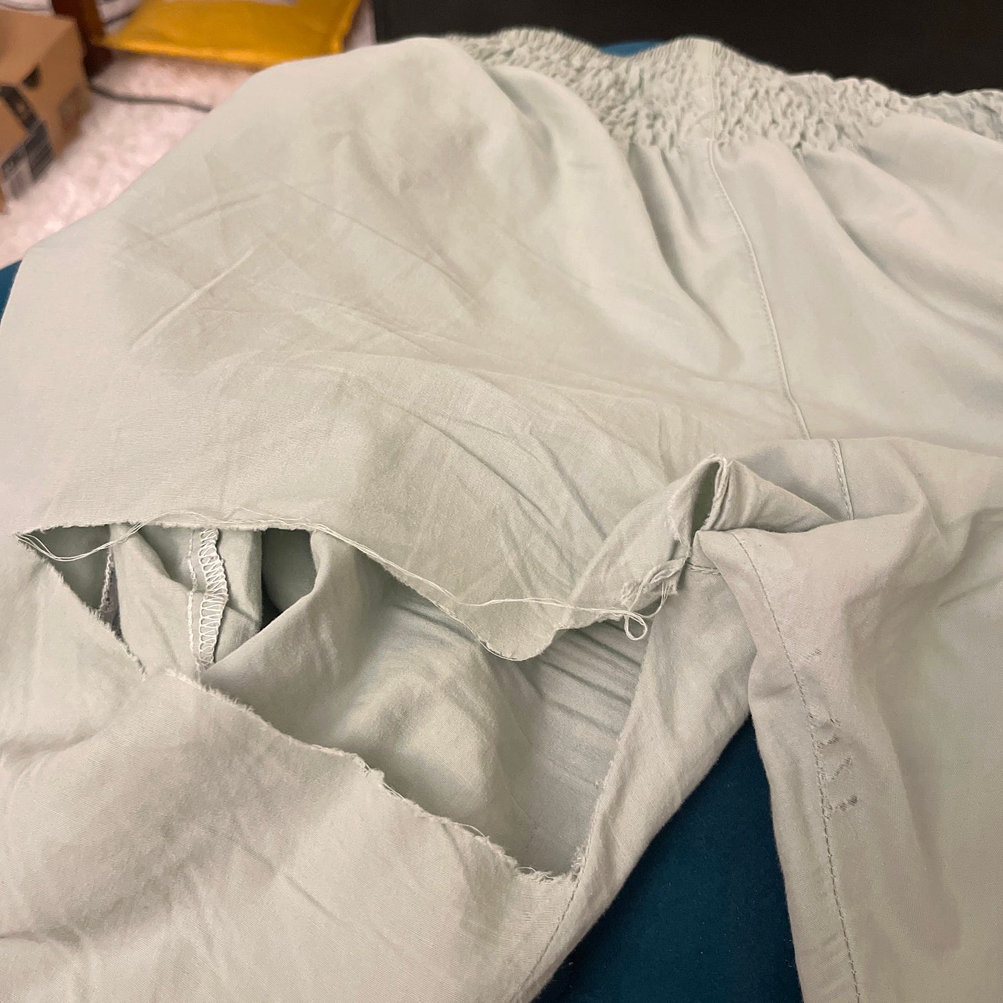 A pair of light green Buddha Pants with a huge hole/tear on the left leg where the thigh meets the butt. A pair of light green Buddha Pants with a huge hole/tear on the left leg where the thigh meets the butt.