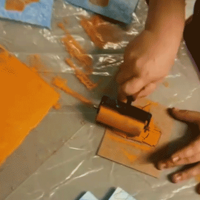 Child's hand pressing inked foam block onto blue paper Hands rolling orange ink onto a brayer Child rolling brayer over foam printing block Hand holding carved foam block with orange ink