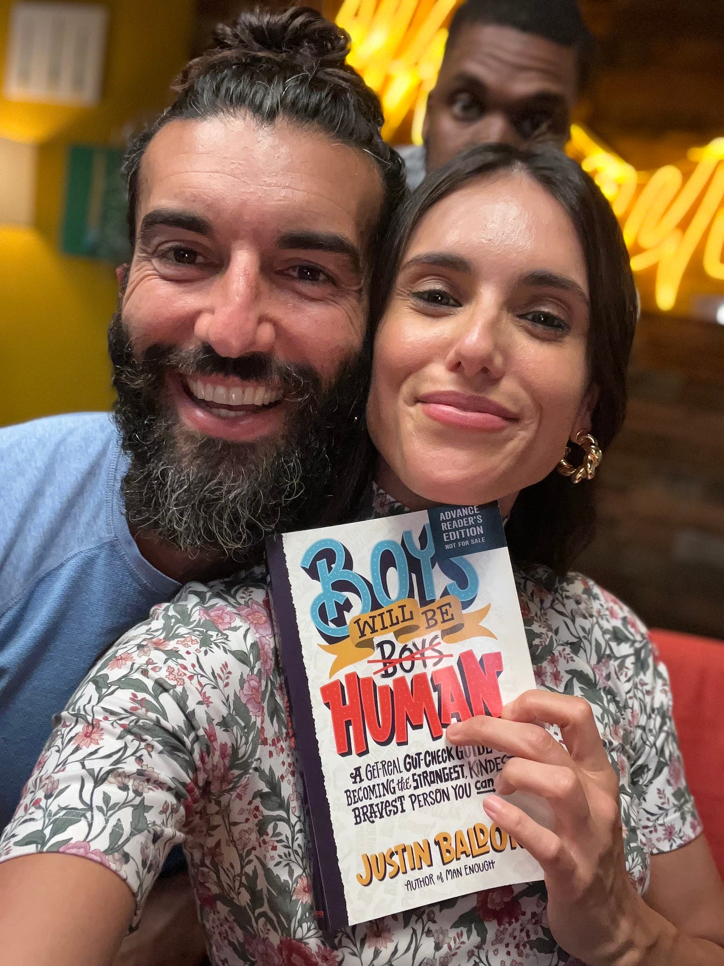 liz wearing flower print shirt holds justin's book and they smile to the camera