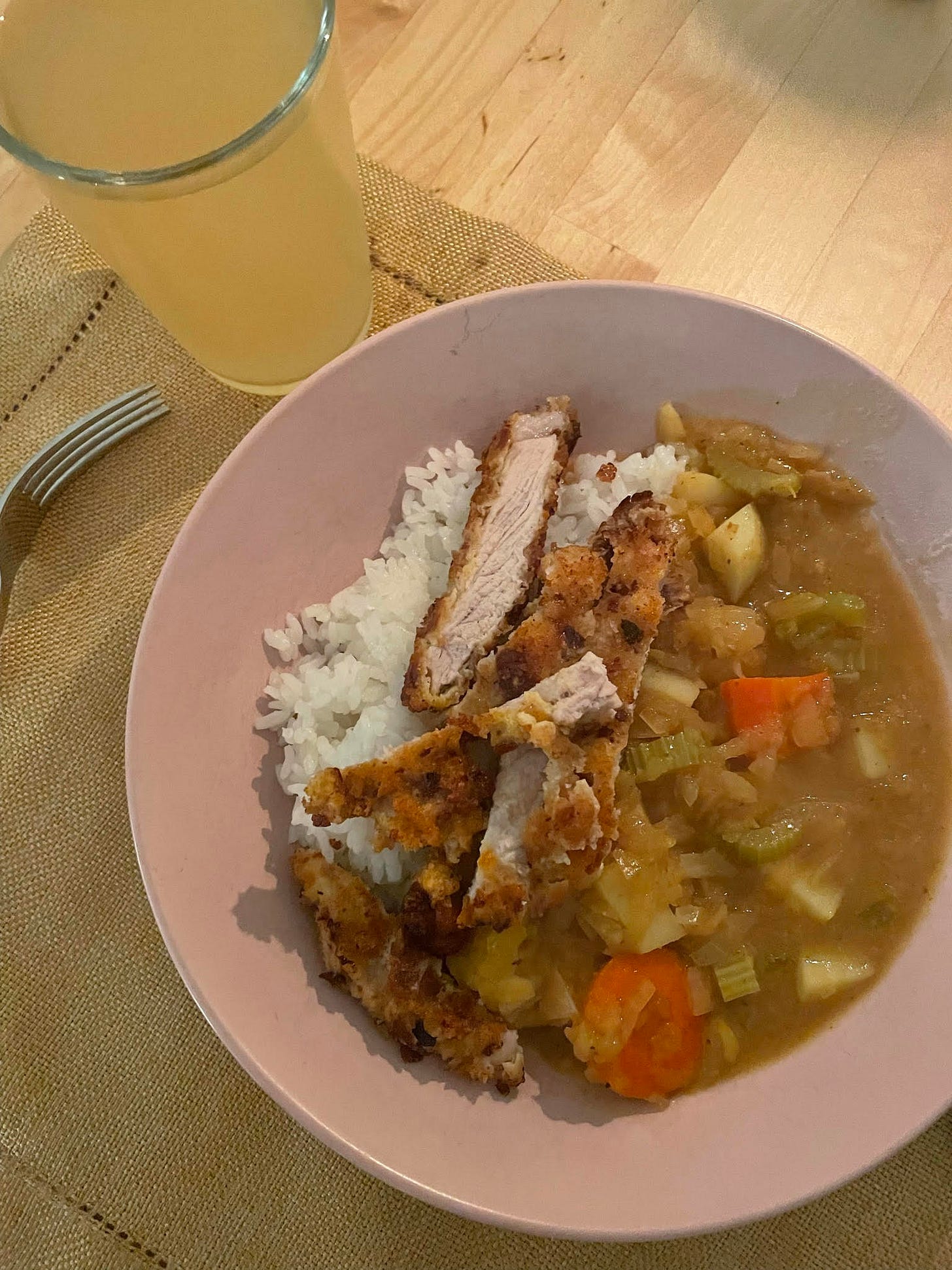 Bowl of rice topped with pork katsu and Japanese curry. A kombuch and fork nearby.