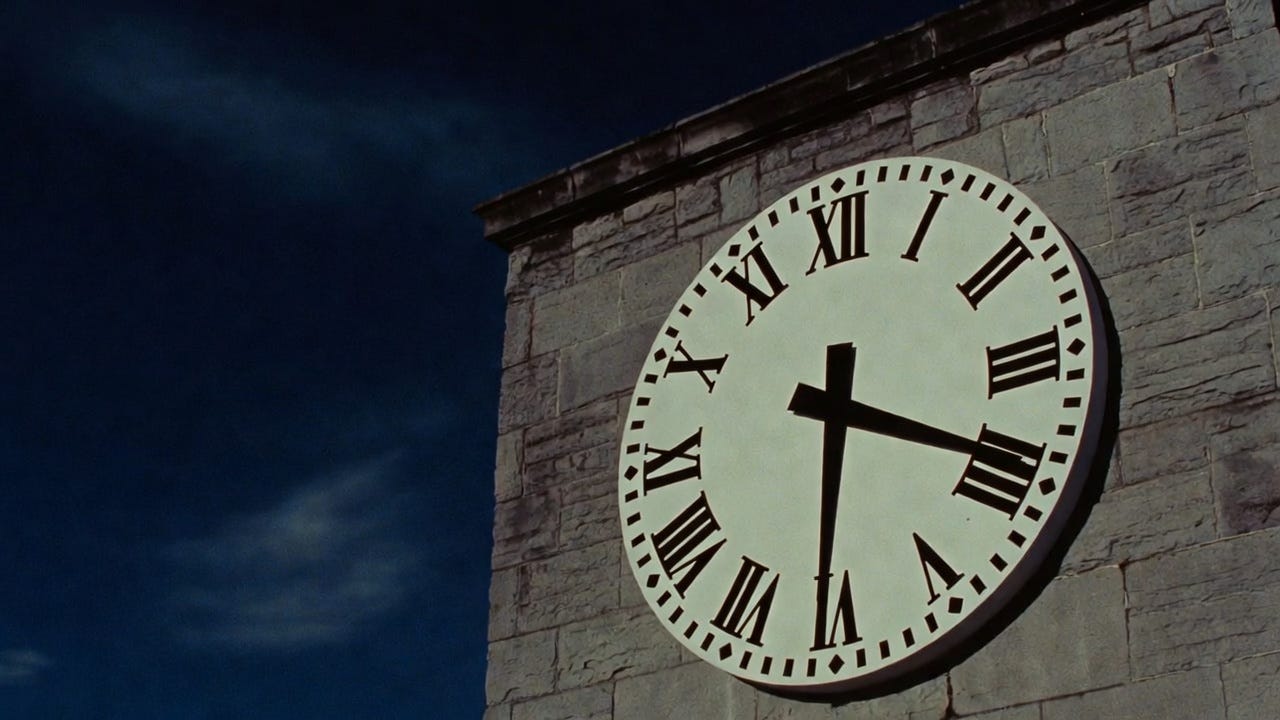 Large analogue wall clock with Roman numerals mounted on a weathered grey stone government building exterior at early evening, time just before midnight, dramatic shadows on the stone under a dark navy sky, centered composition, photorealistic cinematic style with slight film grain. Large analogue wall clock with Roman numerals mounted on a weathered grey stone government building exterior at early evening, time just before midnight, dramatic shadows on the stone under a dark navy sky, centered composition, photorealistic cinematic style with slight film grain.