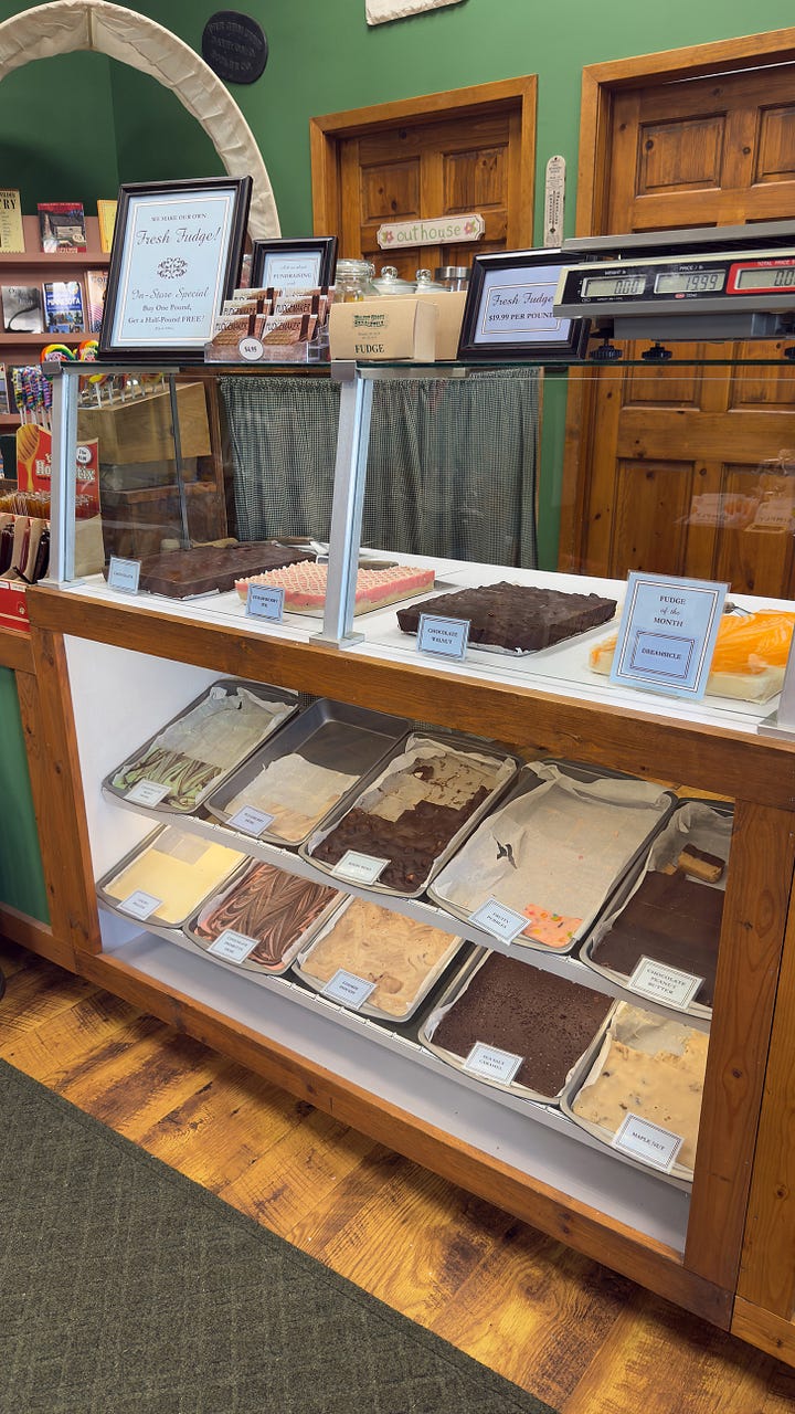 A candy counter with several flavors of fresh fudge. | Kitchen gifts displayed in a kitchen cabinet next to an old stovepipe furnace.