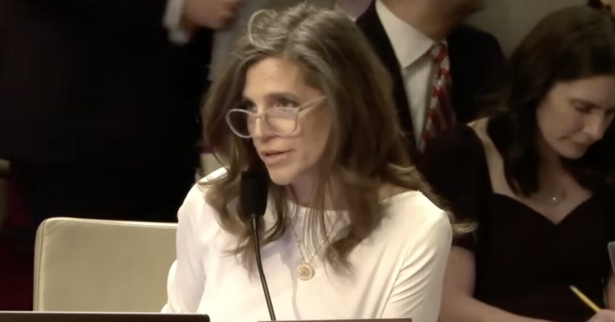 Woman in a white top speaking at a congressional hearing, with attendees in the background engaged in discussions and note-taking. Woman in a white top speaking at a congressional hearing, with attendees in the background engaged in discussions and note-taking.