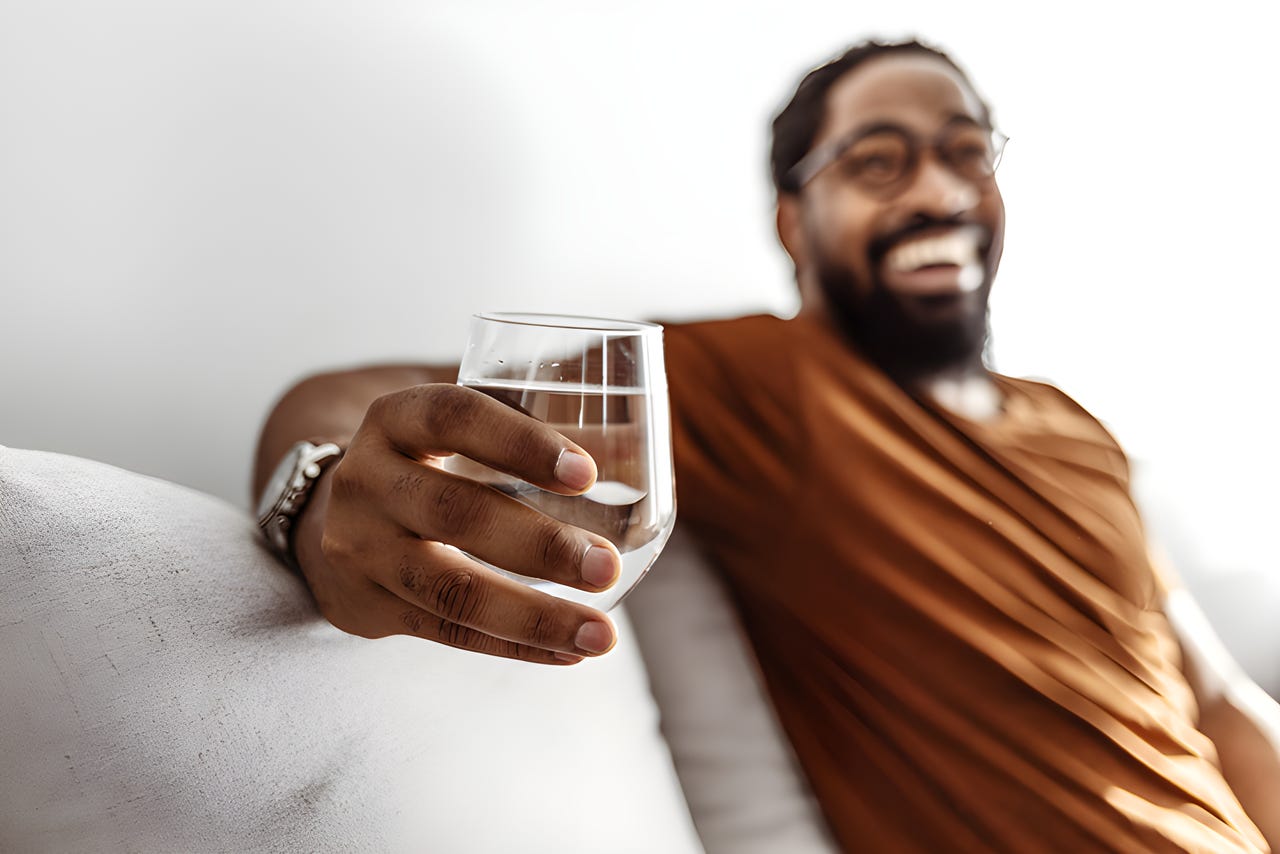 Smiling man sitting on a couch with a glass of water. Smiling man sitting on a couch with a glass of water.