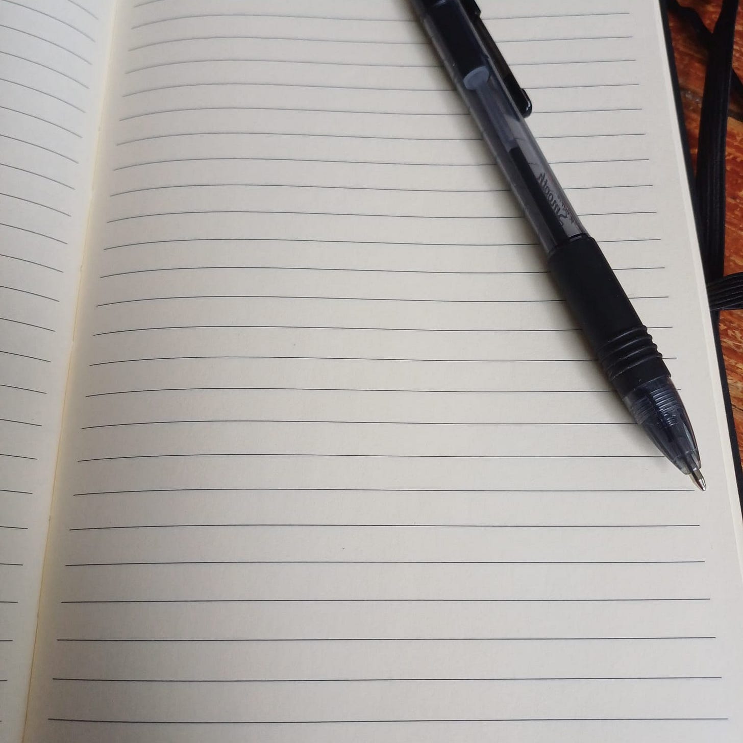 A notebook open with a blank, lined page and a black pen laying on it