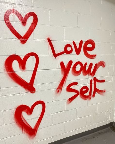 This may contain: graffiti on the wall says love your self and two hearts are drawn in red ink