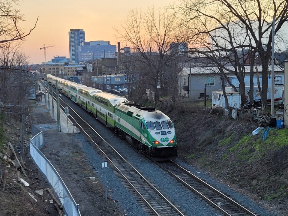 GO Train on tracks with large buildings seen in the background against a sunset. GO Train on tracks with large buildings seen in the background against a sunset.