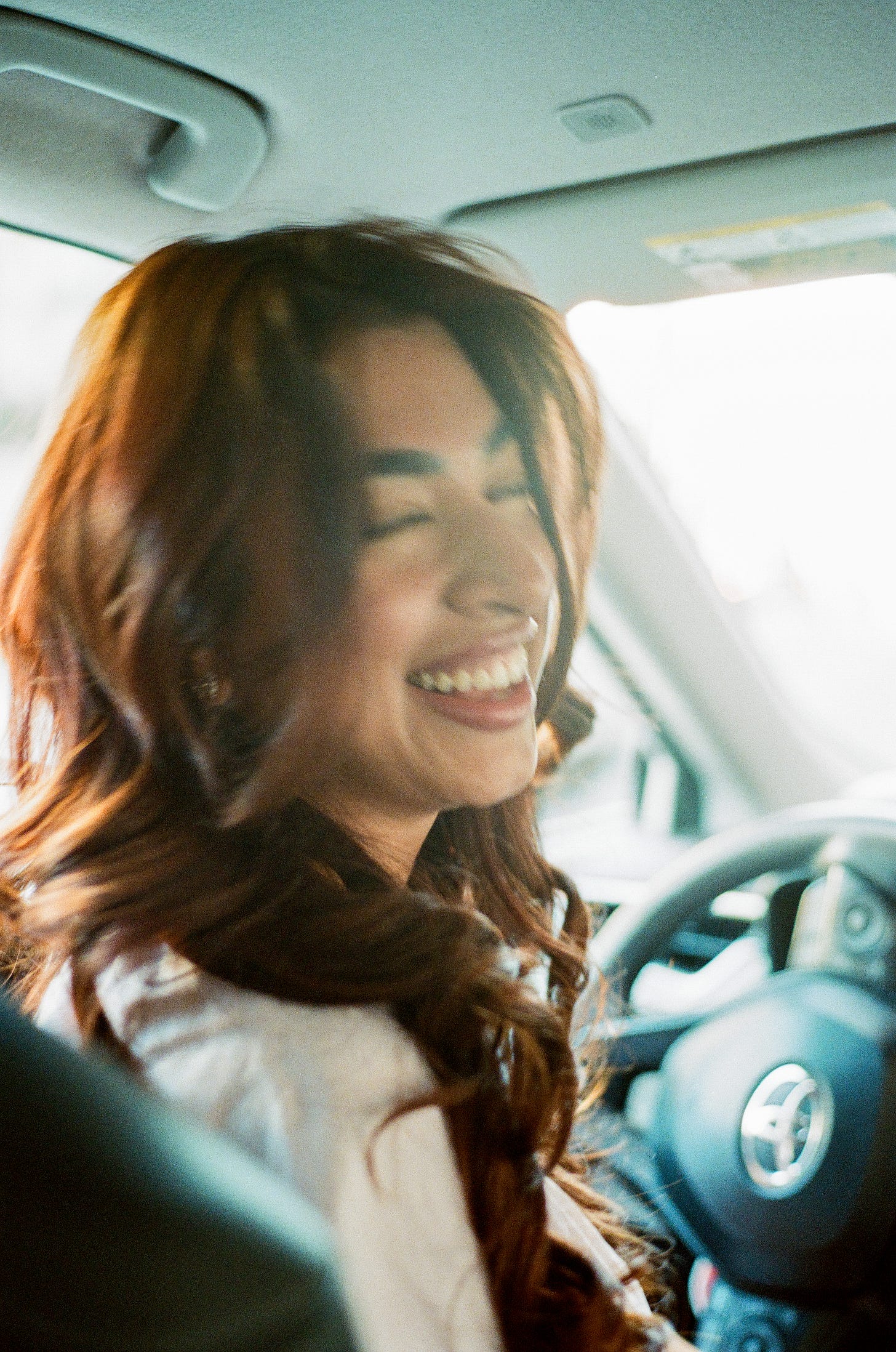 My lovely Lyft driver laughing bathed in light streaming through the windshield