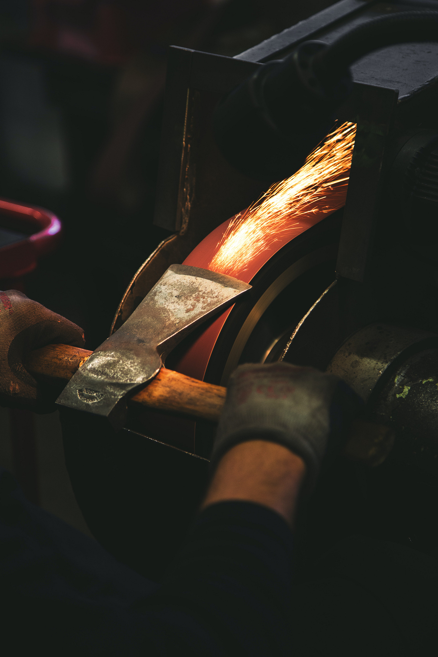 Someone in gloves grinding the blade of an axe with sparks flyingforward into the mechanism
