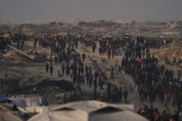Crowds of people walking across a dusty landscape with the edges of tents in the foreground.