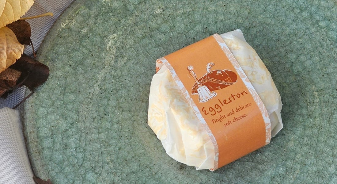 A green plate with a soft cheese with an orange wrapper on it A green plate with a soft cheese with an orange wrapper on it