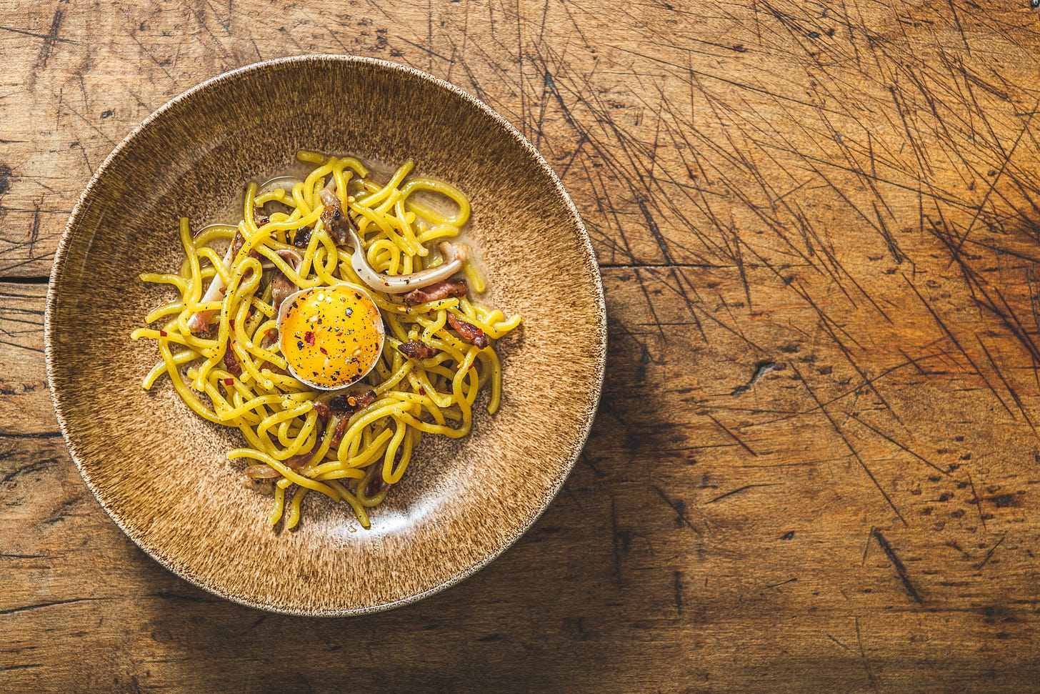 a brown bowl on a wooden table filled with Carbonara at Peasant restaurant