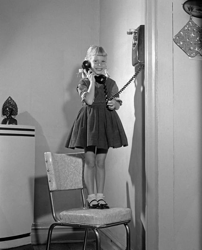 1960s-1950s Young Girl Standing On Kitchen Chair Looking At Camera Talking On Wall Telephone Print By Vintage Collection