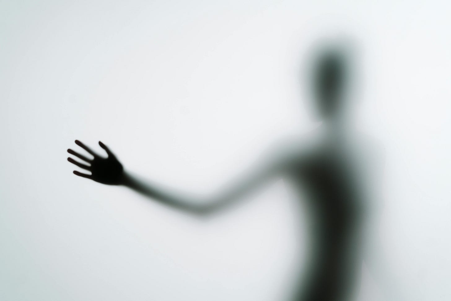 Blurred silhouette of a person with an outstretched hand against a light gray background, creating a mysterious and ethereal mood.