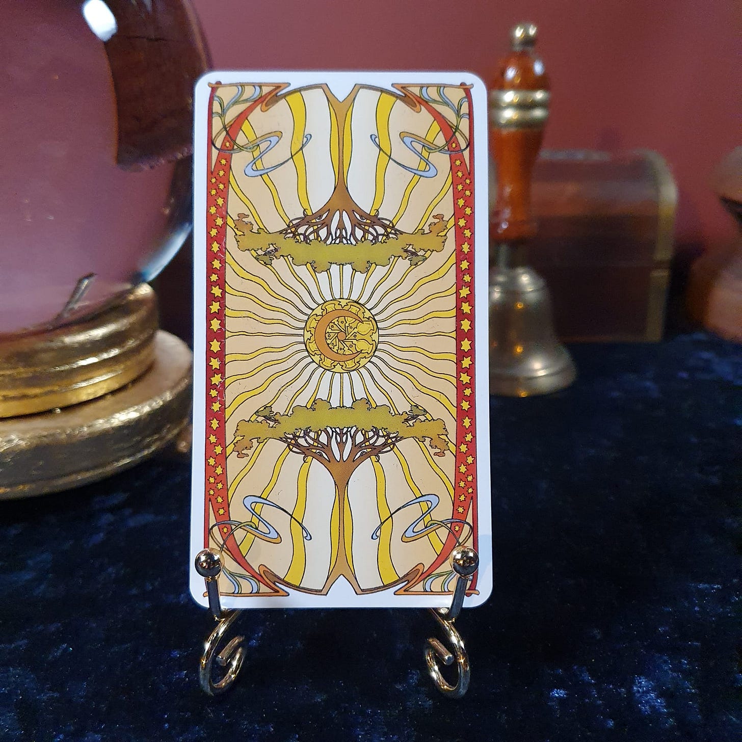 Decorative tarot card back with sun, tree and art nouveau-style pattern displayed on a stand for the Elspeth Wilson Tarot DMs interview.