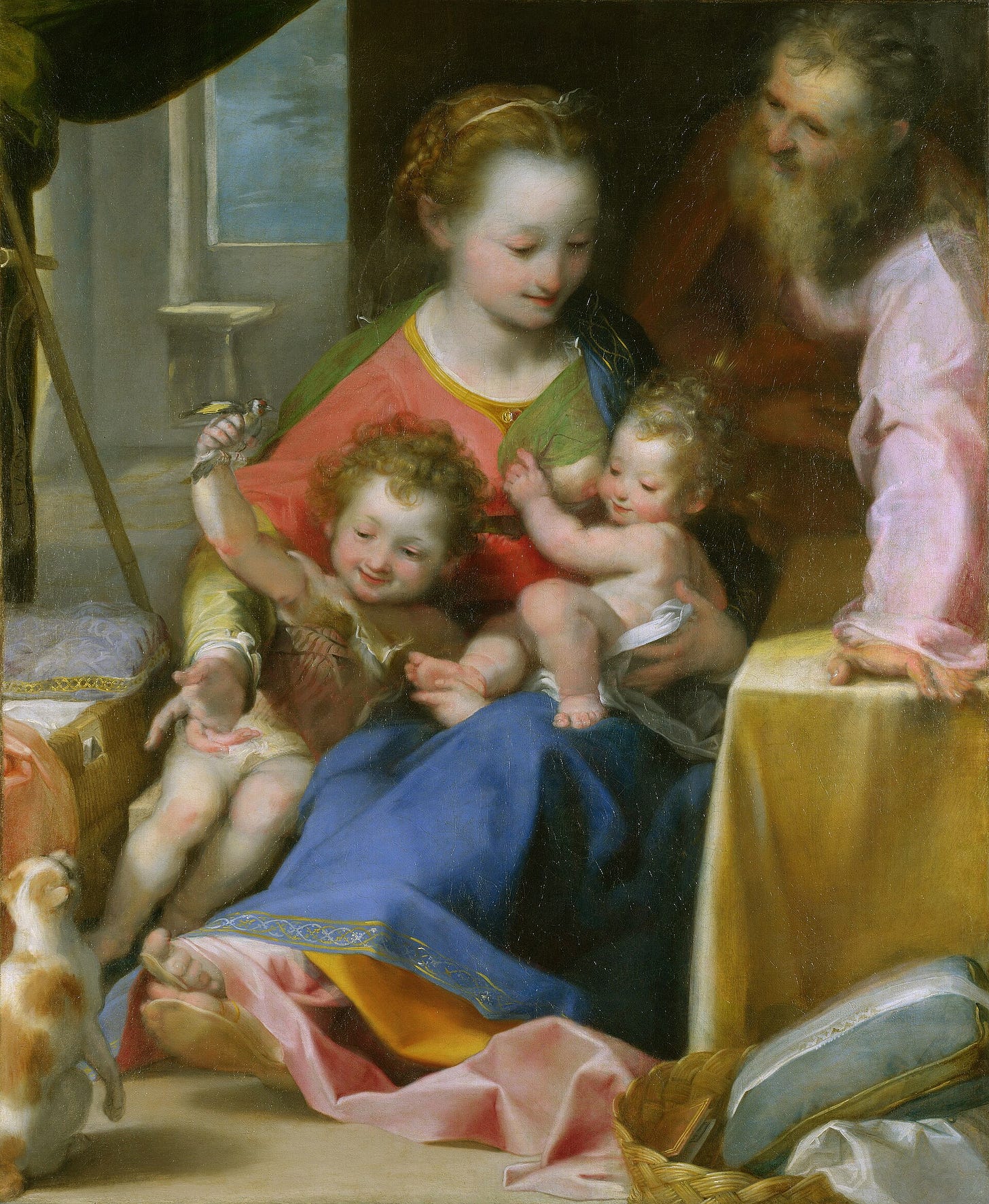 In a bedroom, Mary nurses the infant Jesus while the young John the Baptist holds a goldfinch above a cat sitting on its haunches, and Joseph leans in from behind, smiling.