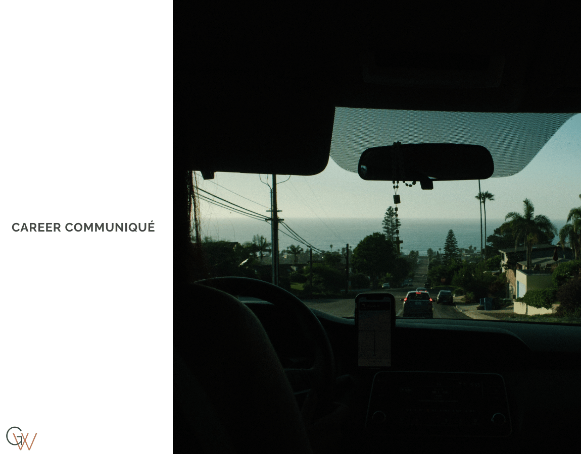 The view from inside a car before dawn, a phone mount visible on the dashboard, the back seat partially visible, and an early morning street stretching toward a pale horizon through the windshield. The view from inside a car before dawn, a phone mount visible on the dashboard, the back seat partially visible, and an early morning street stretching toward a pale horizon through the windshield.