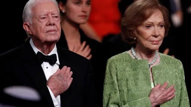 Former U.S. President Jimmy Carter and his wife Rosalynn hold their right hands on their chests at a ceremony