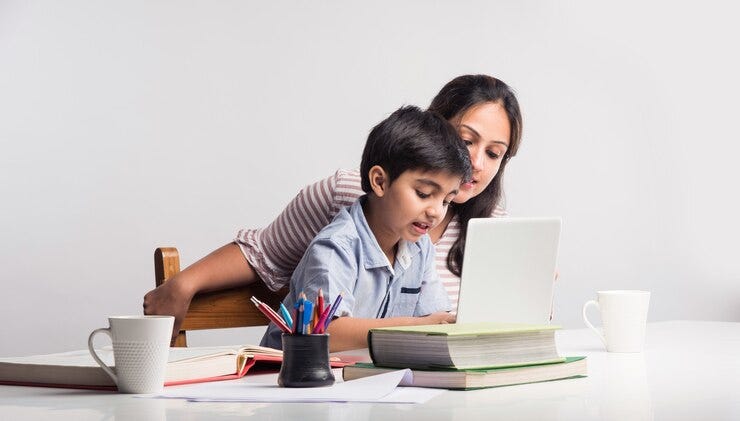 Cute Indian boy with mother doing homework at home using laptop and books - online schooling concept