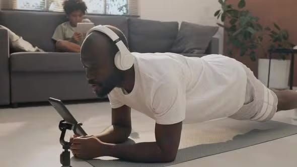 man wearing all white doing plank exericse while working with fitness trainer on phone. man wearing all white doing plank exericse while working with fitness trainer on phone.