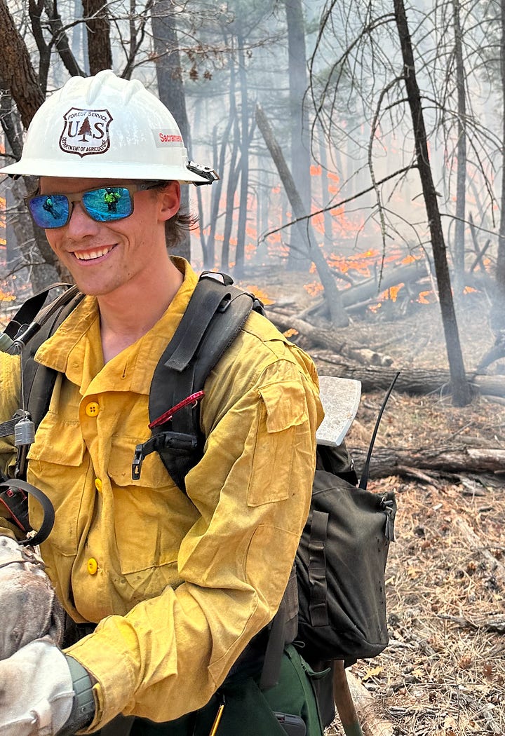 young man in fire uniform poses in front of a red engine. young firefighter in a burning forest in a national forest helmet 