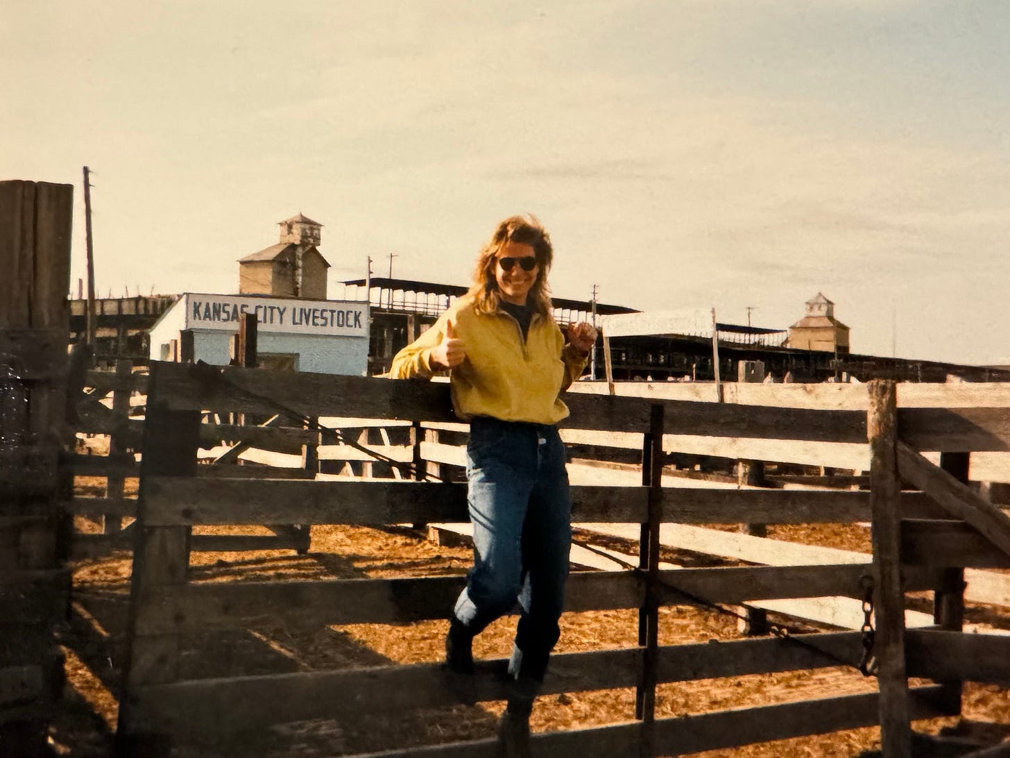 A woman with a mullet and sunglasses stands in front of a cattle fence. A woman with a mullet and sunglasses stands in front of a cattle fence.