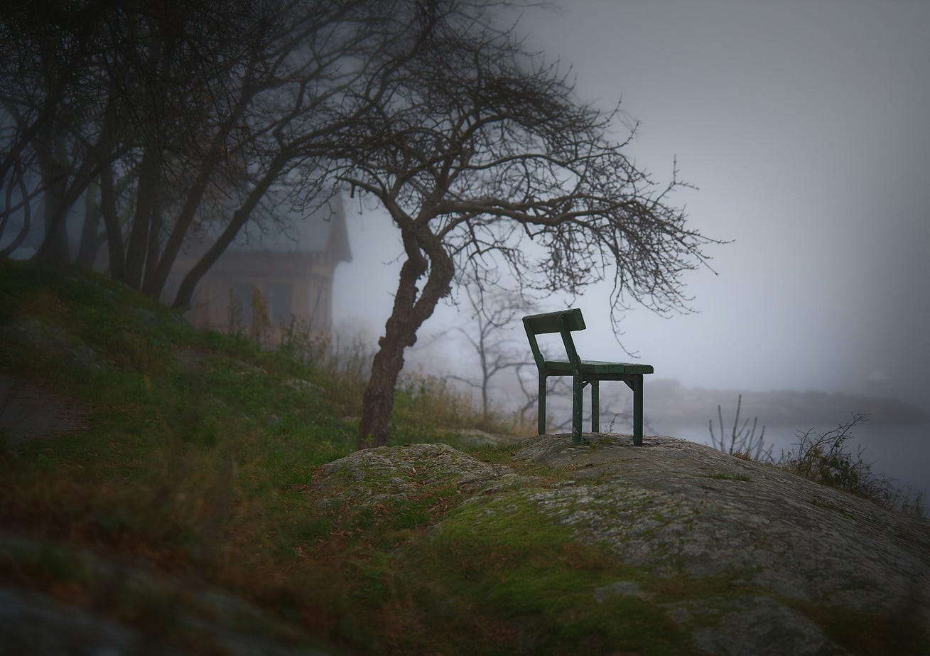 A dark image of a dull green chair on a rock by the water- a building to the left in the haze. A dark image of a dull green chair on a rock by the water- a building to the left in the haze.