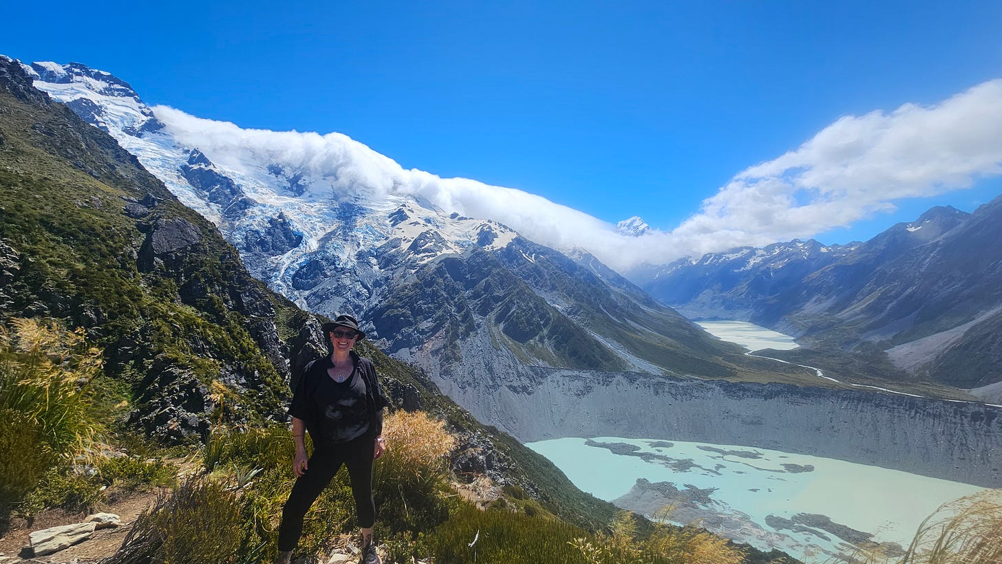 Caucasian woman stands at Top of Sealy Tarns Track, view of Aoraki/Mount Cook in background
