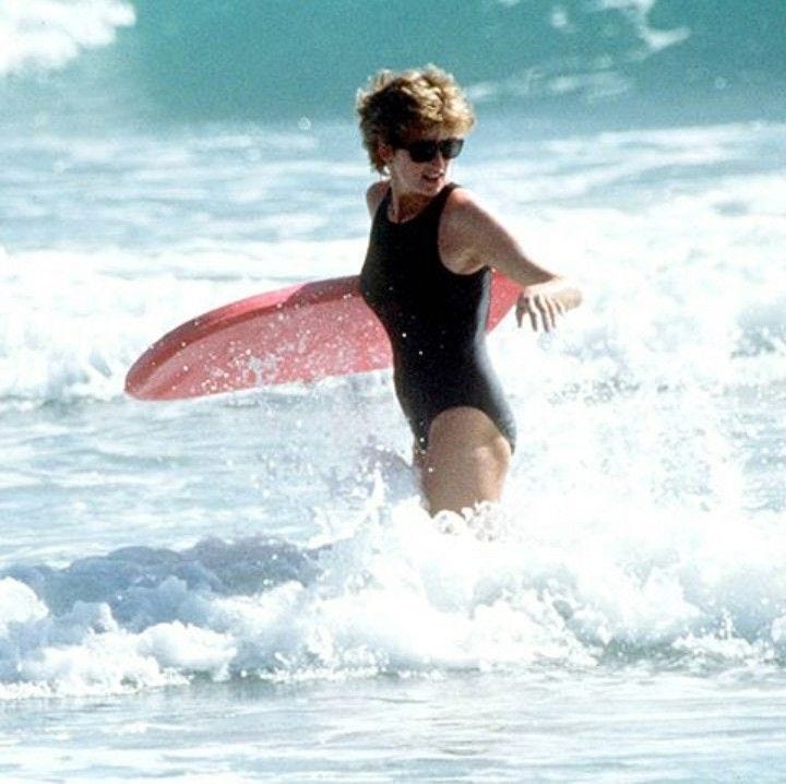 This may contain: a woman in a black swimsuit carrying a red surfboard through the ocean waves