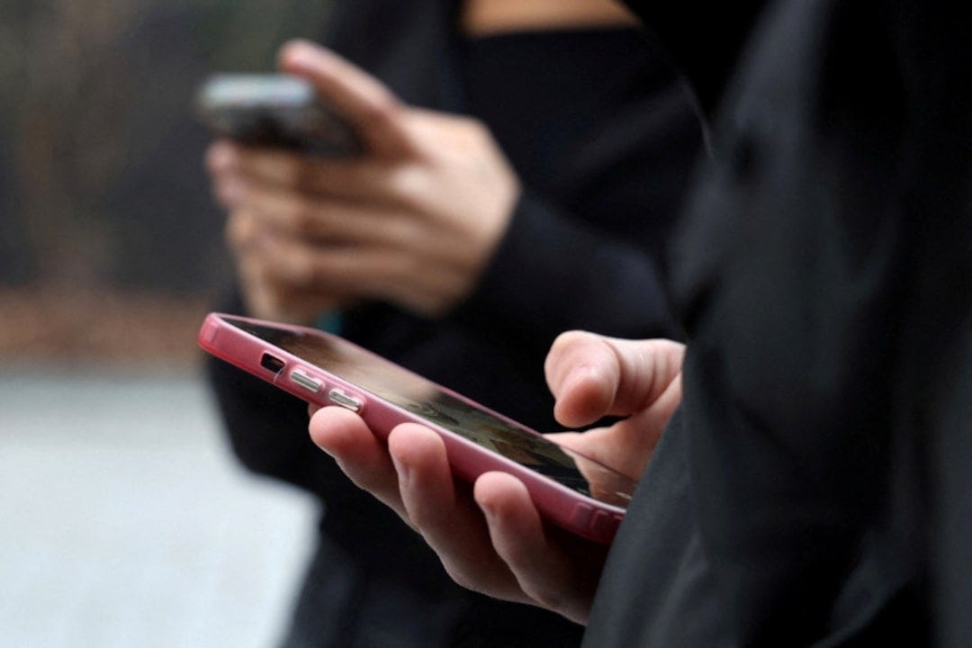Teenagers look at their mobile phone screens in Paris Teenagers look at their mobile phone screens in Paris