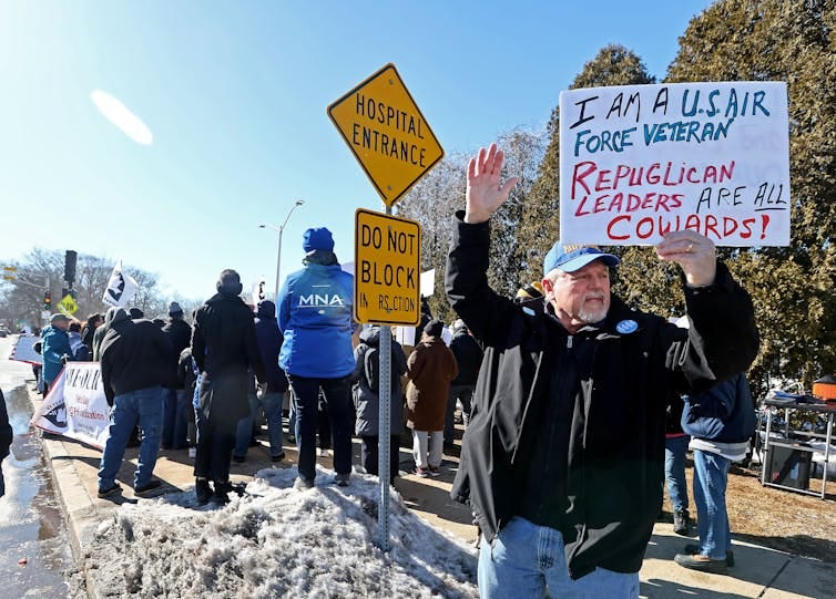 A man standing with a sign that says 'I'm a USAIR Force veteran Republican leaders are all cowards!' A man standing with a sign that says 'I'm a USAIR Force veteran Republican leaders are all cowards!'