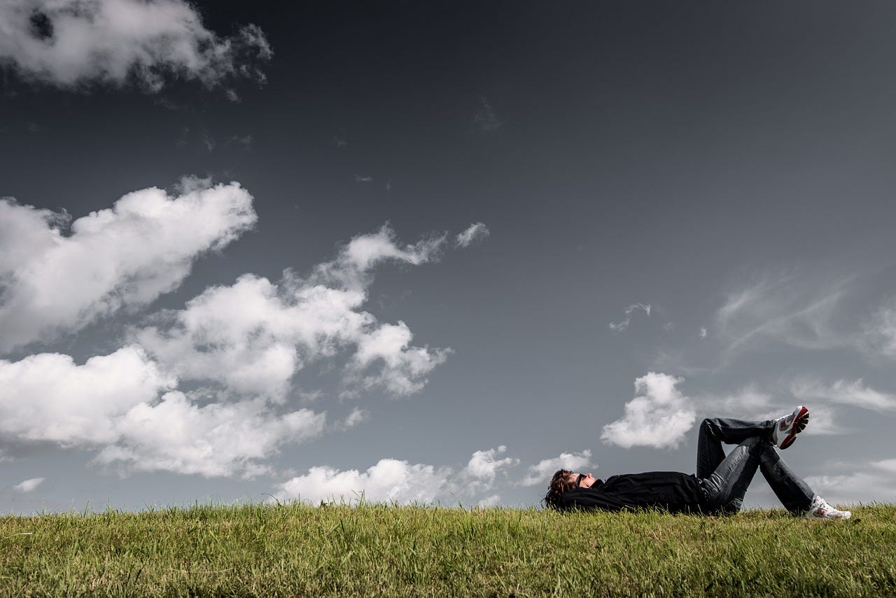 Person laying on grass, puffy clouds in blue sky above