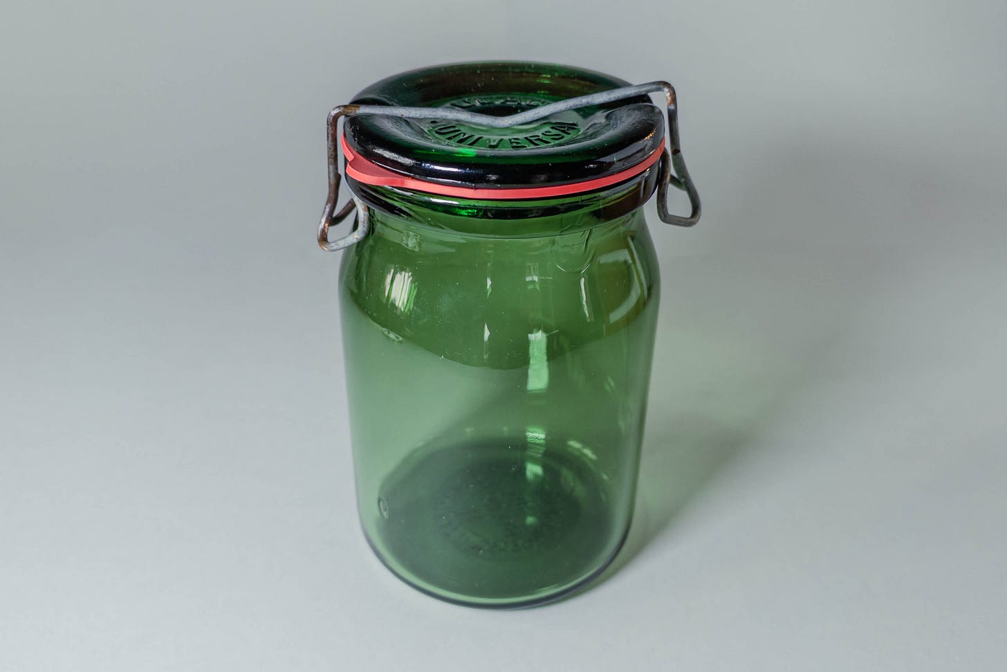 Green Buelach preserving jar with glass lid, orange rubber ring, and metal swing clamp; the lid bears the embossed word “Universal,” like it’s quietly claiming to solve all kitchen problems. Green Buelach preserving jar with glass lid, orange rubber ring, and metal swing clamp; the lid bears the embossed word “Universal,” like it’s quietly claiming to solve all kitchen problems.