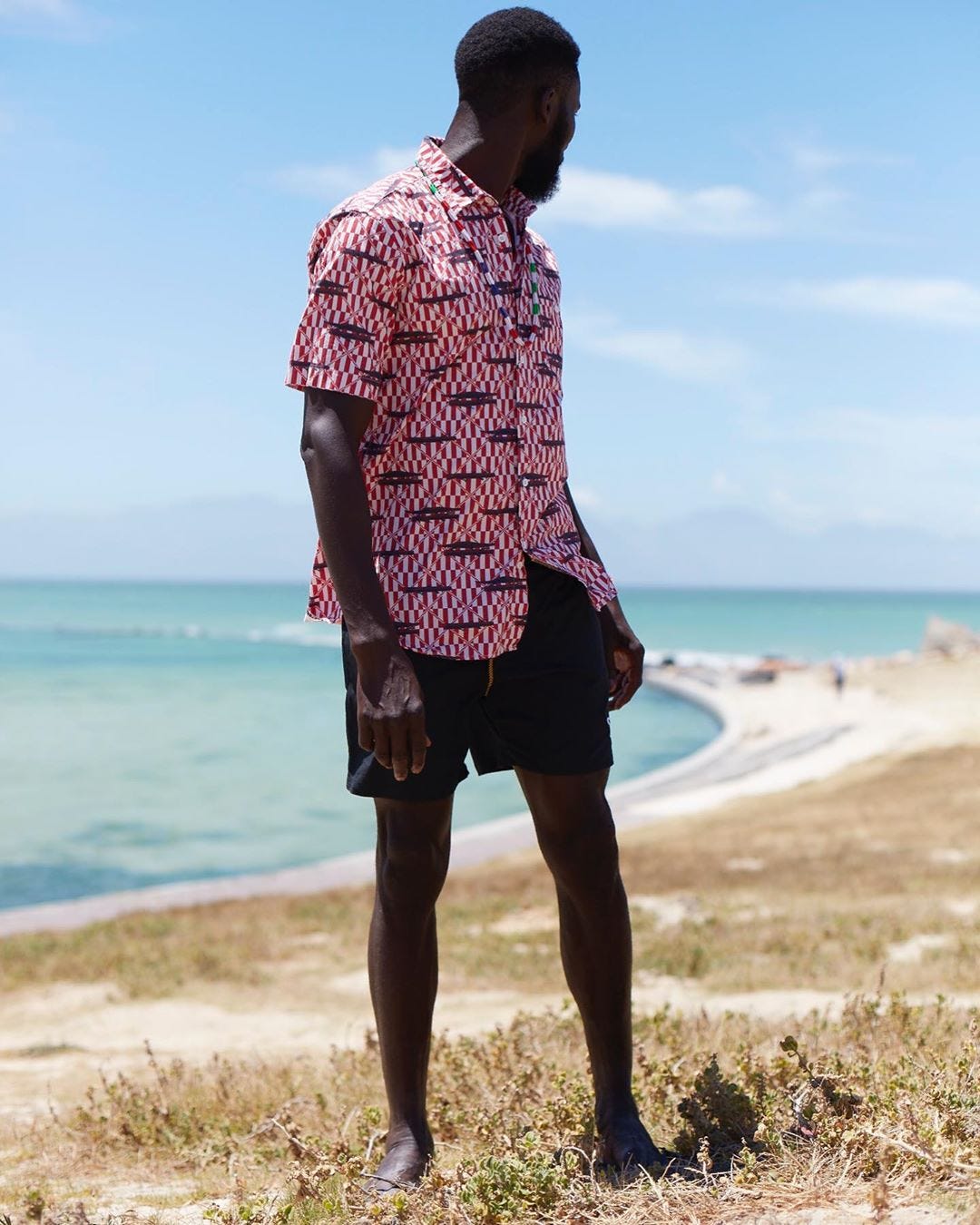 a black man stands triumphantly on a beachside cliff wearing a mami wata shirt
