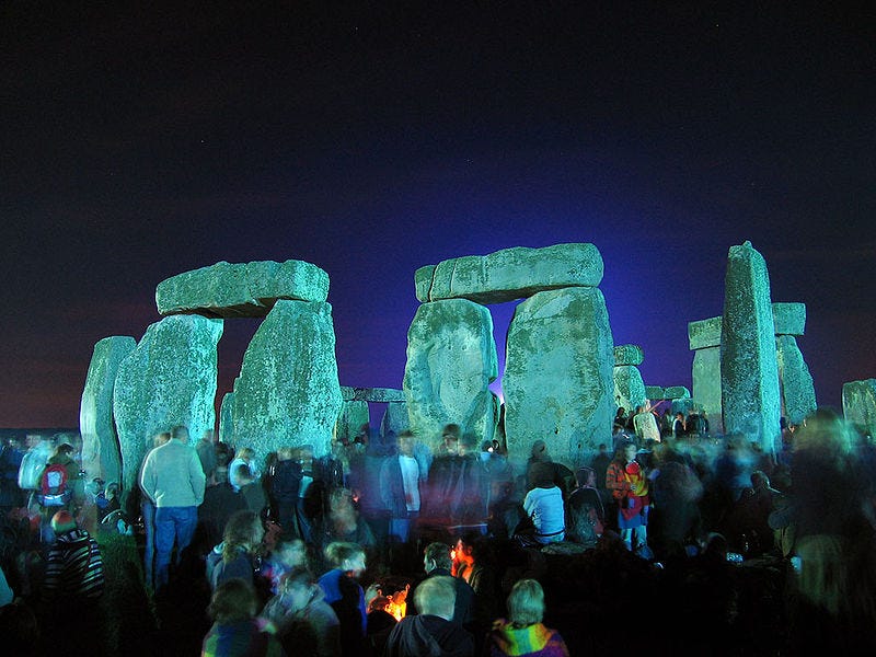 A group of people standing around stonehenge

Description automatically generated